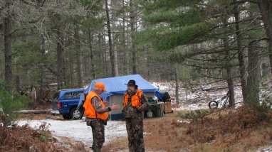 Two men wearing blaze orange in front of a hunting camp.