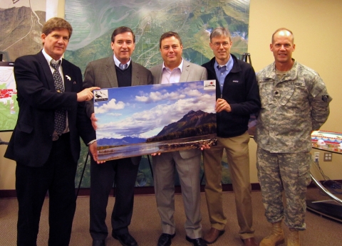 Five men stand with a beautiful image of Alaska's coastline. 