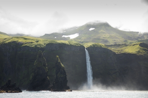 A green island with a large waterfall over a cliff into the water.