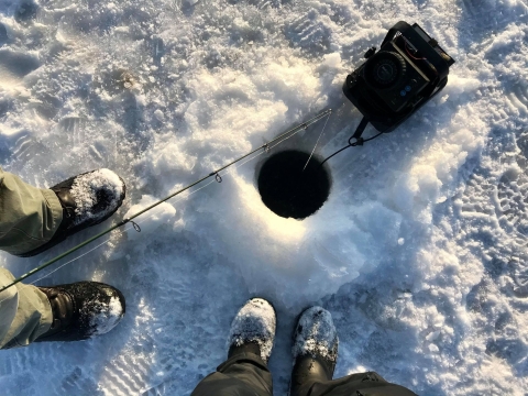 two people looking down at a hole in the ice