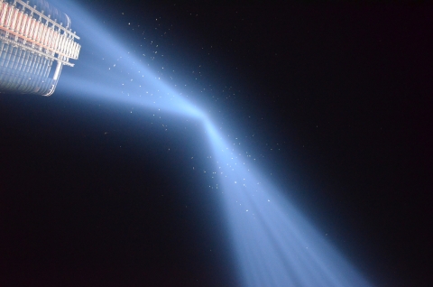 Two blue beams of light lighting up the night sky. A cluster of birds are seen flying in the beams. 