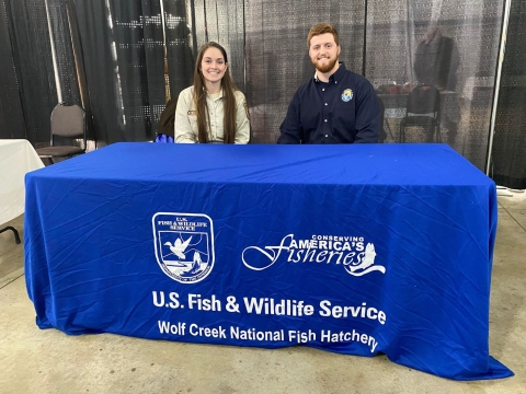 USFWS employee and volunteer sitting behind blue information booth