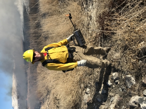 man in hardhat with drip torch; smoke in background