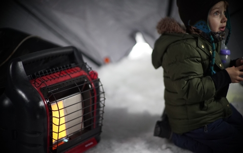 a boy sits on the ice in a shack near a heater