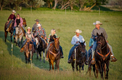 Nine people ride together on horseback on a grassland