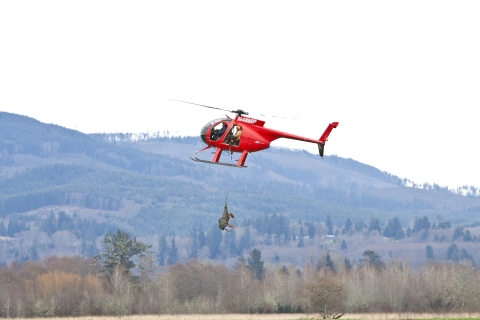 Red helicopter lifts what looks like a mammal off the ground.
