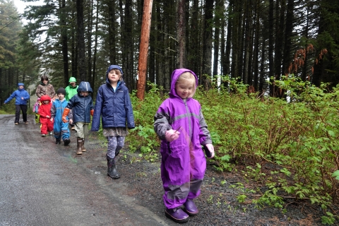 kids in multicolored rain gear walk down a gravel road