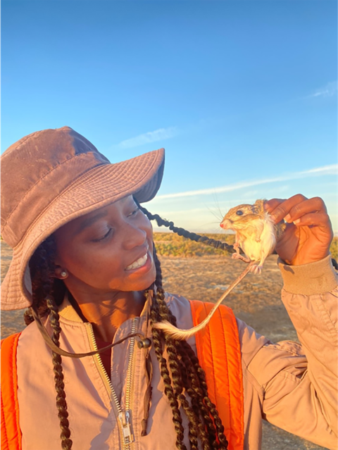 A woman wearing a brown hat and holding a small rodent