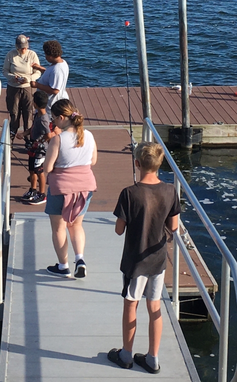youth line up on a boardwalk to have their fishing rods set up by a fish biologist