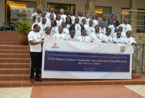 A group of adult students stand behind a banner on steps.