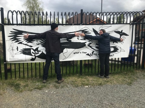 a man and a woman stand against a banner that show different bird silhouttes so they can measure their wingspan
