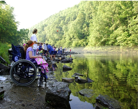 A line of children fishing along a riverbank 