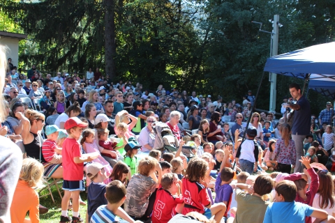 Children in a large outdoor audience raise their hands to volunteer in a wildlife demonstration 