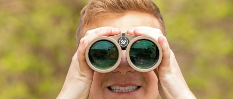 A red-haired boy looks at the camera through binoculars.