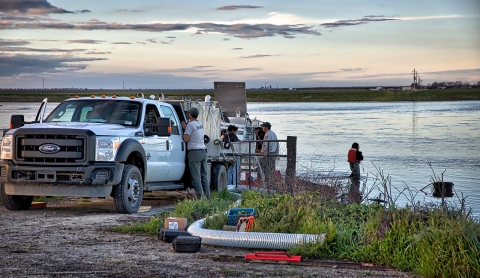 A truck, people and equipment by a river