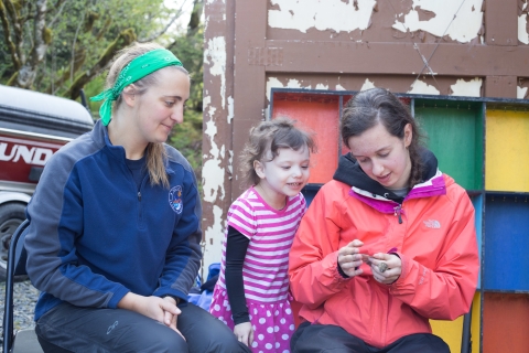A young woman measures a small birds wing while another woman and young girl observe