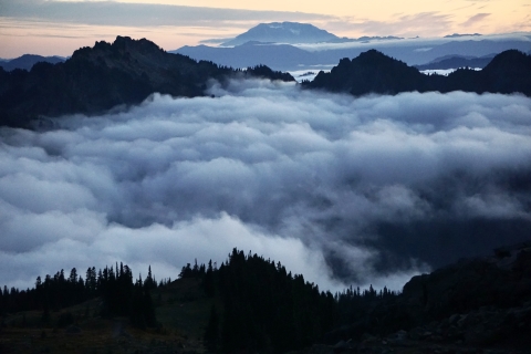 Clouds rest in valleys leading to a distant mountain at dusk