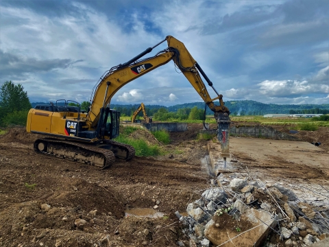 Heavy equipment on a dirt landscape with green vegetation and blue skies above