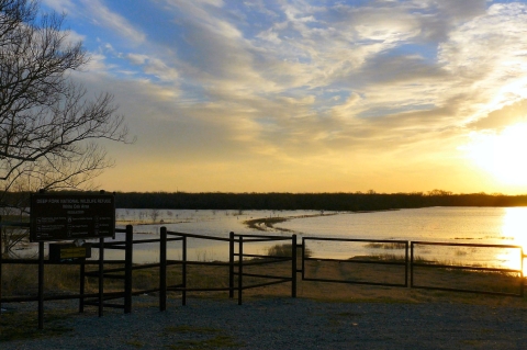 An observation deck looks out onto a body of water during a sunset.