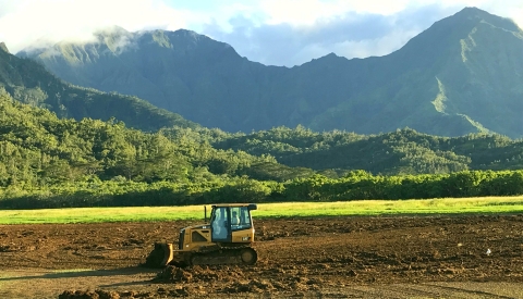 A dozer levels brown earth. Behind it are dramatic green mountains.