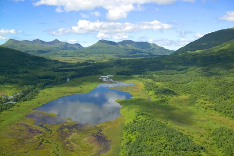 Clouds reflect in a wetland surrounded by mountains.