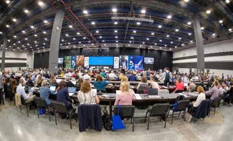 A large meeting space with people sitting at long tables