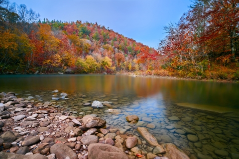 A lovely river with a rock bank on both sides. In the background the trees are various vibrant fall colors. 