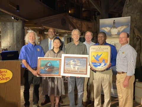Group photo of people holding duck stamp arts and USFWS logo.