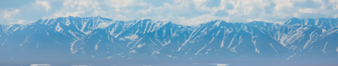 A person works at the edge of a wetland before mountain range and beneath partly cloudy skies.