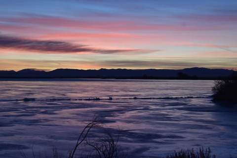 Early sunrise colors over a lake, with dark mountains in the distance