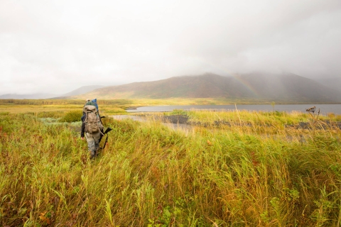 Two hunters with backpacks and firearms walk through Kodiak National Wildlife Refuge