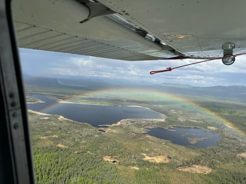 view of a rainbow over a landscape under an airplane wing