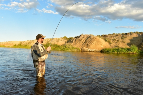 Person standing in refuge lake holding fly fishing pole.