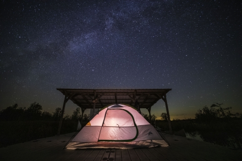 Lit up tent on a platform with half of a roof underneath a night sky full of stars