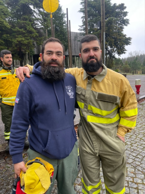 Two firefighters stand together and pose for a photo with their arms around each other.
