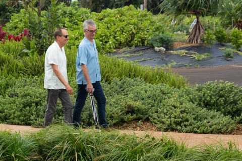 Two older men walk down a path surrounded by lush greenery