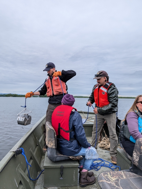 Three researchers in a boat drop a ponar dredge over the side to sample for dreissenid mussels. 