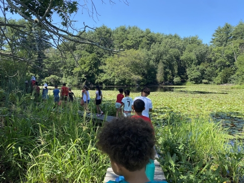 young kids walk on a boardwalk beside a body of water
