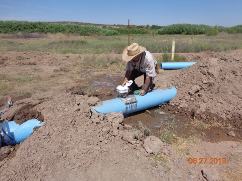 A USFWS staff member checks the meter on a pipe in a field