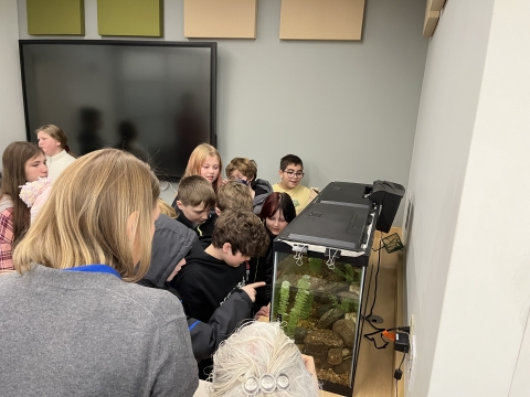 a group of elementary school students and Service staff stand huddled around a large aquarium tank filled with young eels
