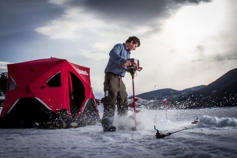 Photo of ice fisherman drilling a hole through the ice on a frozen lake