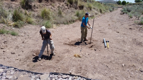 Two individuals setting up equipment in a dry field