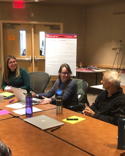 Three individuals sit around a desk having a discussion
