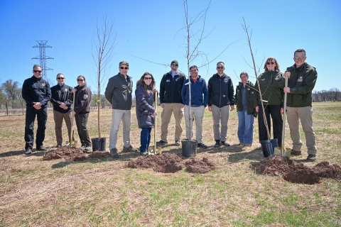 A group of people standing with trees and holes dug in a field.