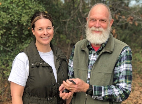 Two people pose for a photo. The one on the right has a small dark colored snake in his hands.