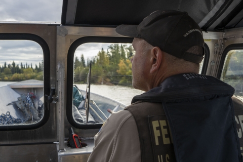 close up of a unformed officer drives a boat with a river in the background