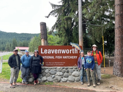 A group of six stands by the Leavenworth National Fish Hatchery entrance sign