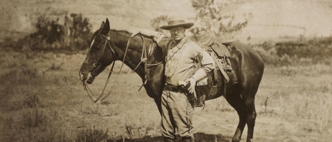 President Theodore Roosevelt poses with his horse on a prairie