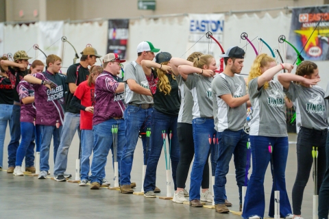 Young archery target shooters aim at targets from the shooting line. 
