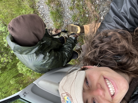 Biologist smiling while lifting a boot up to have friend clean dirt out of tread. 